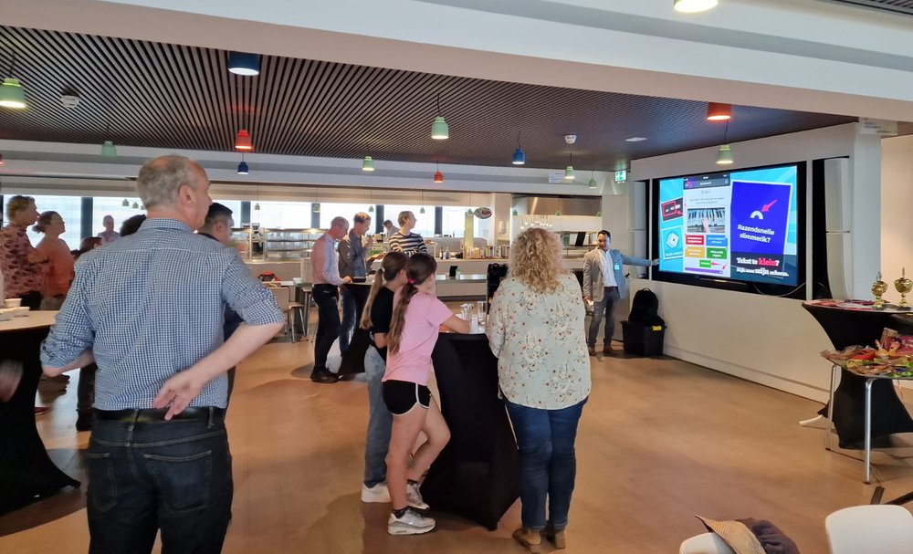 Colleagues and their children follow a security awareness quiz on the big screen at the NS office